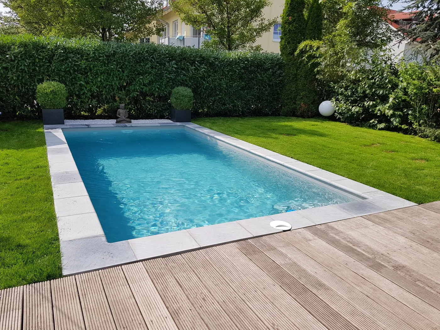Gartenpool mit Holzdeck und weißer Einfassung im Rasen